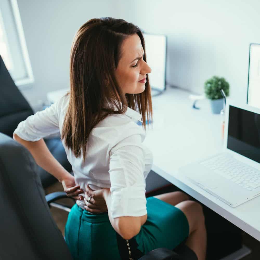 Woman sitting at her desk in Rockville MD holding her back in pain.