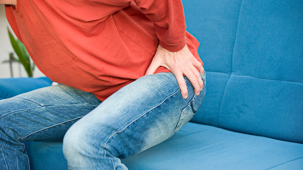 man sitting on blue couch holding hip because he is in hip pain from hip labral tear