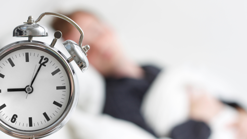 picture of alarm clock on bed in front of man sleeping
